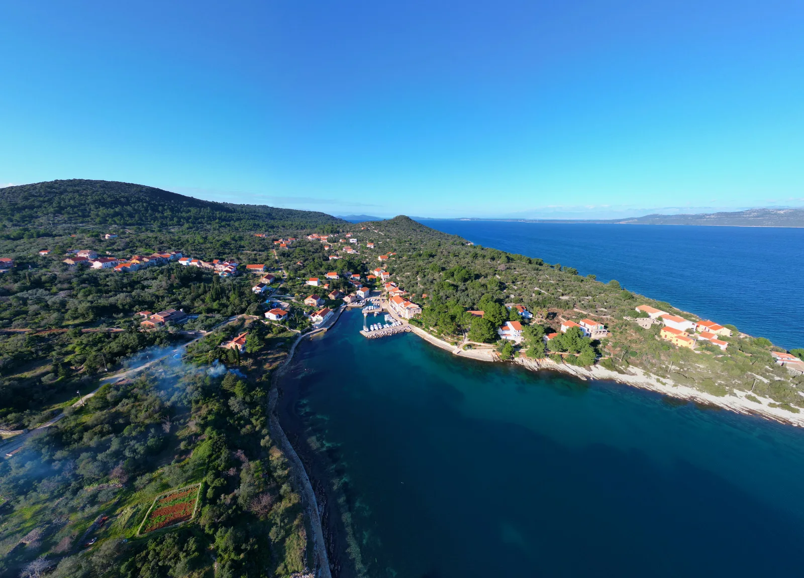 Discover the serene village of Veli Iž on Croatia's coastline, captured from above with clear skies and lush greenery.