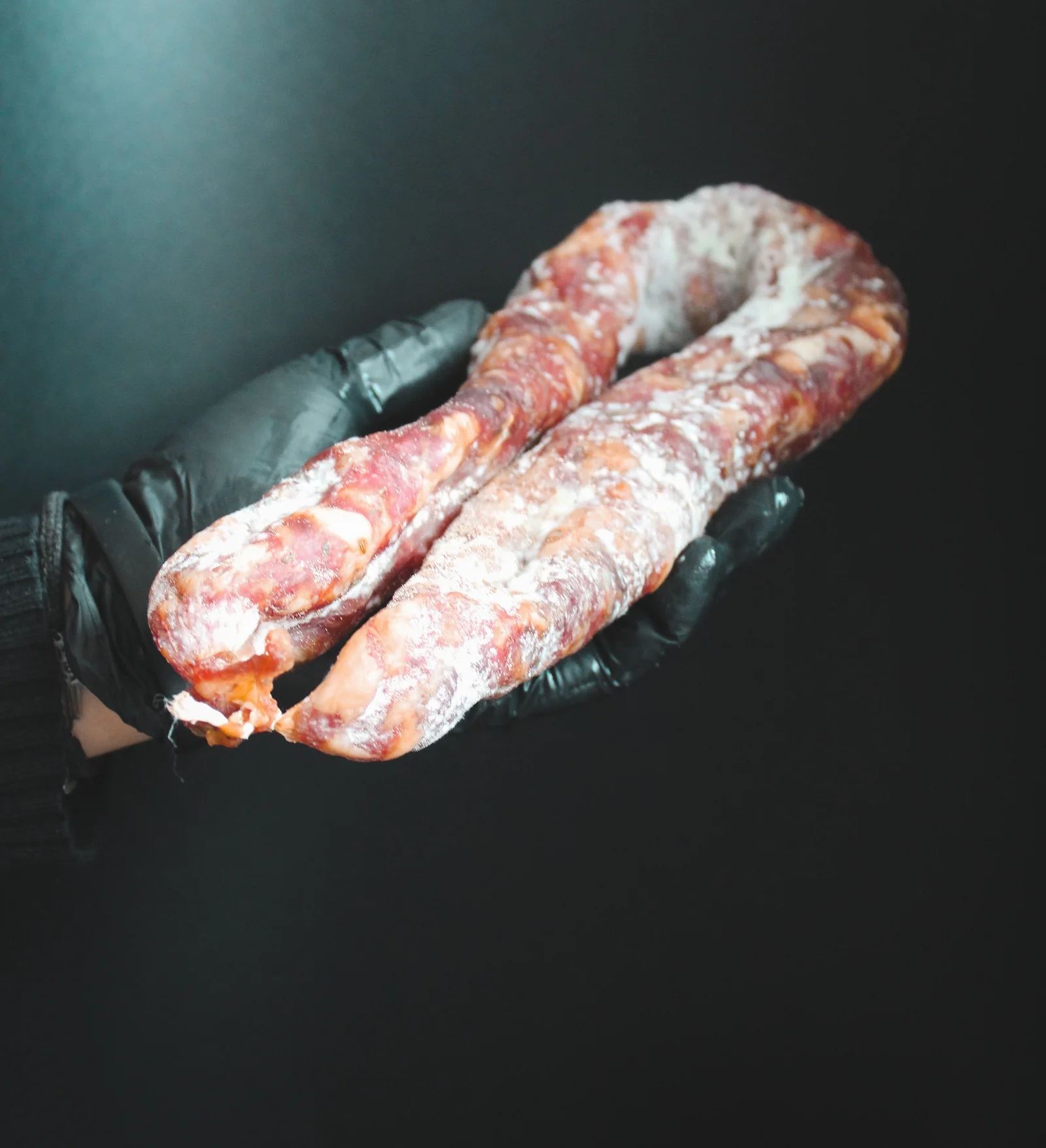 Frozen raw sausages held in gloved hands against a dark background.