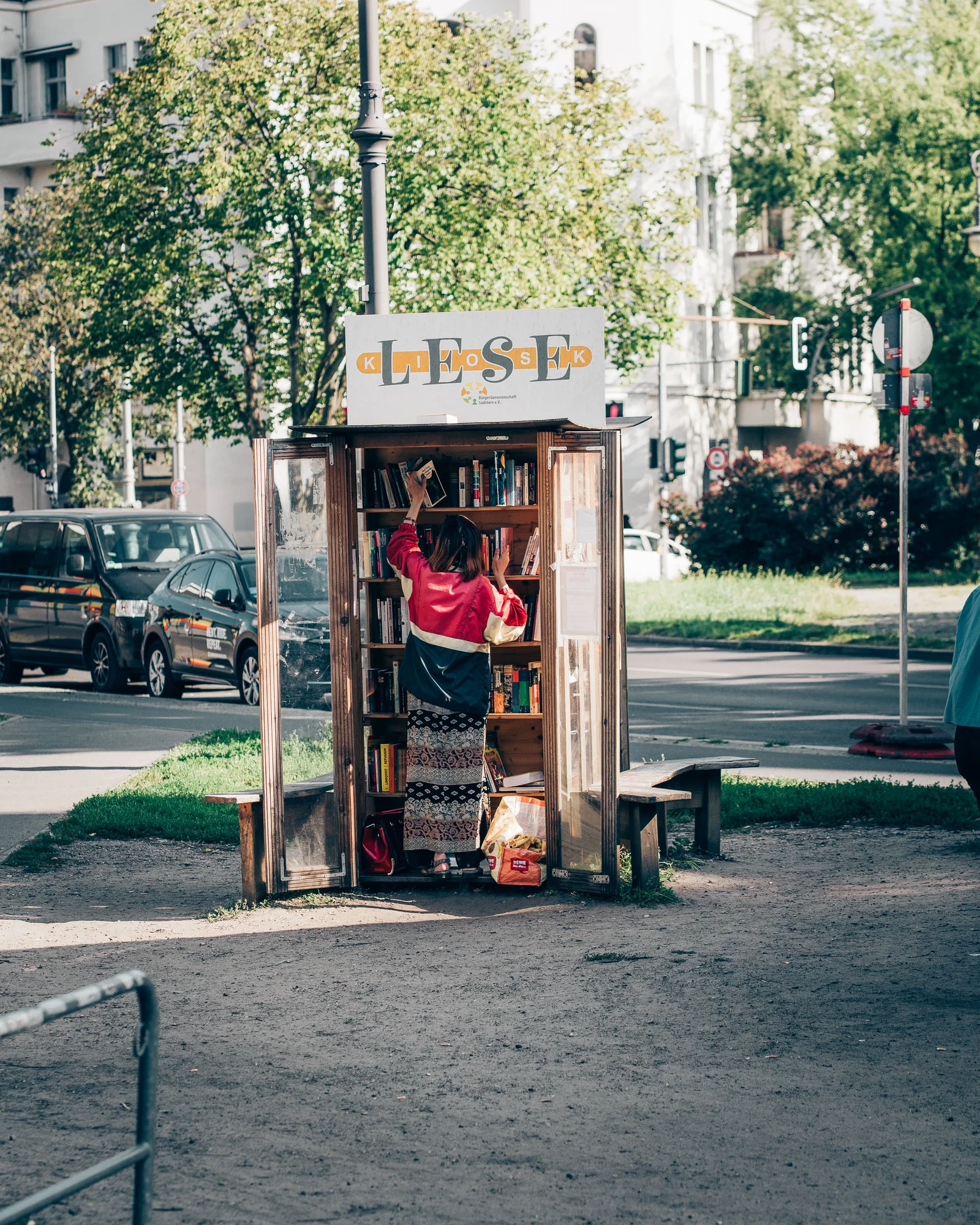 A person browsing books at a street library in Kreuzberg, Berlin on a sunny day.