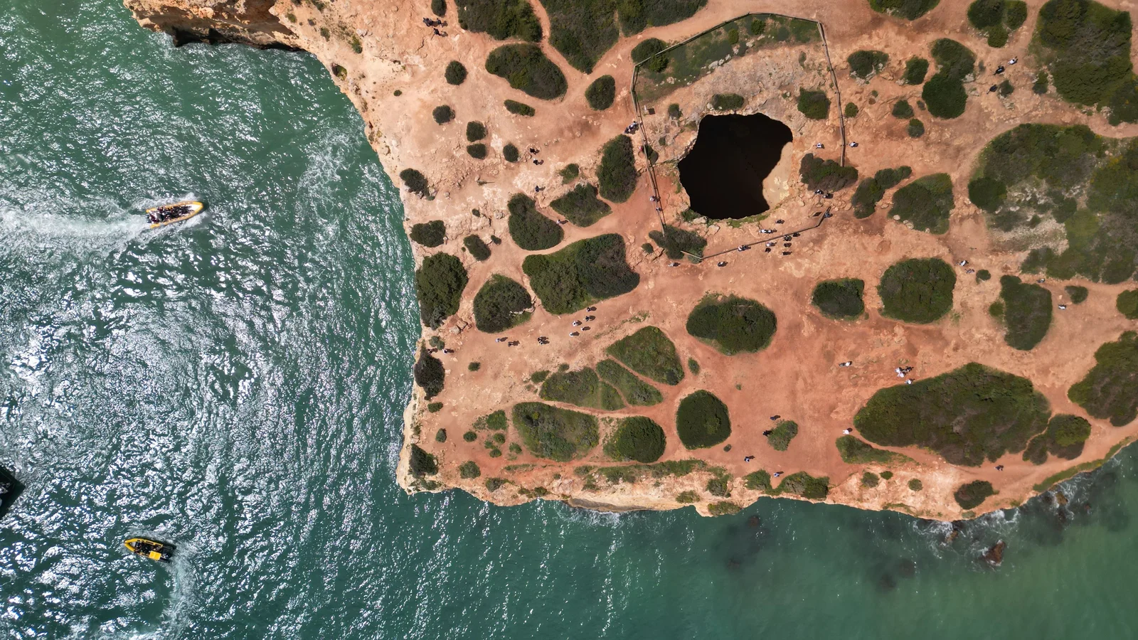 Dramatic aerial shot of the Algarve coastline in Portugal featuring a natural cave and clear waters.
