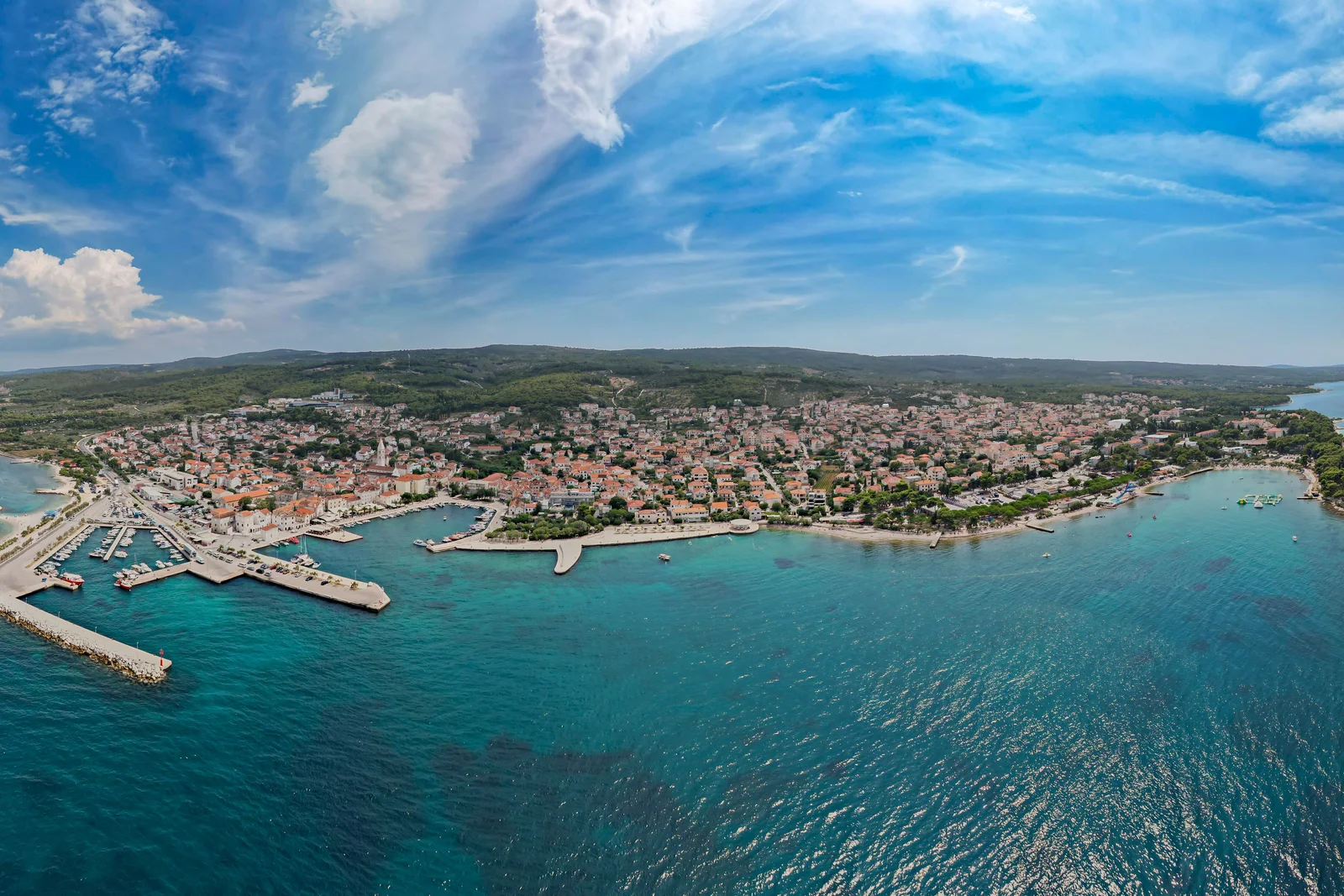 Panoramic aerial view of a scenic coastal town with bustling harbor and clear blue waters.