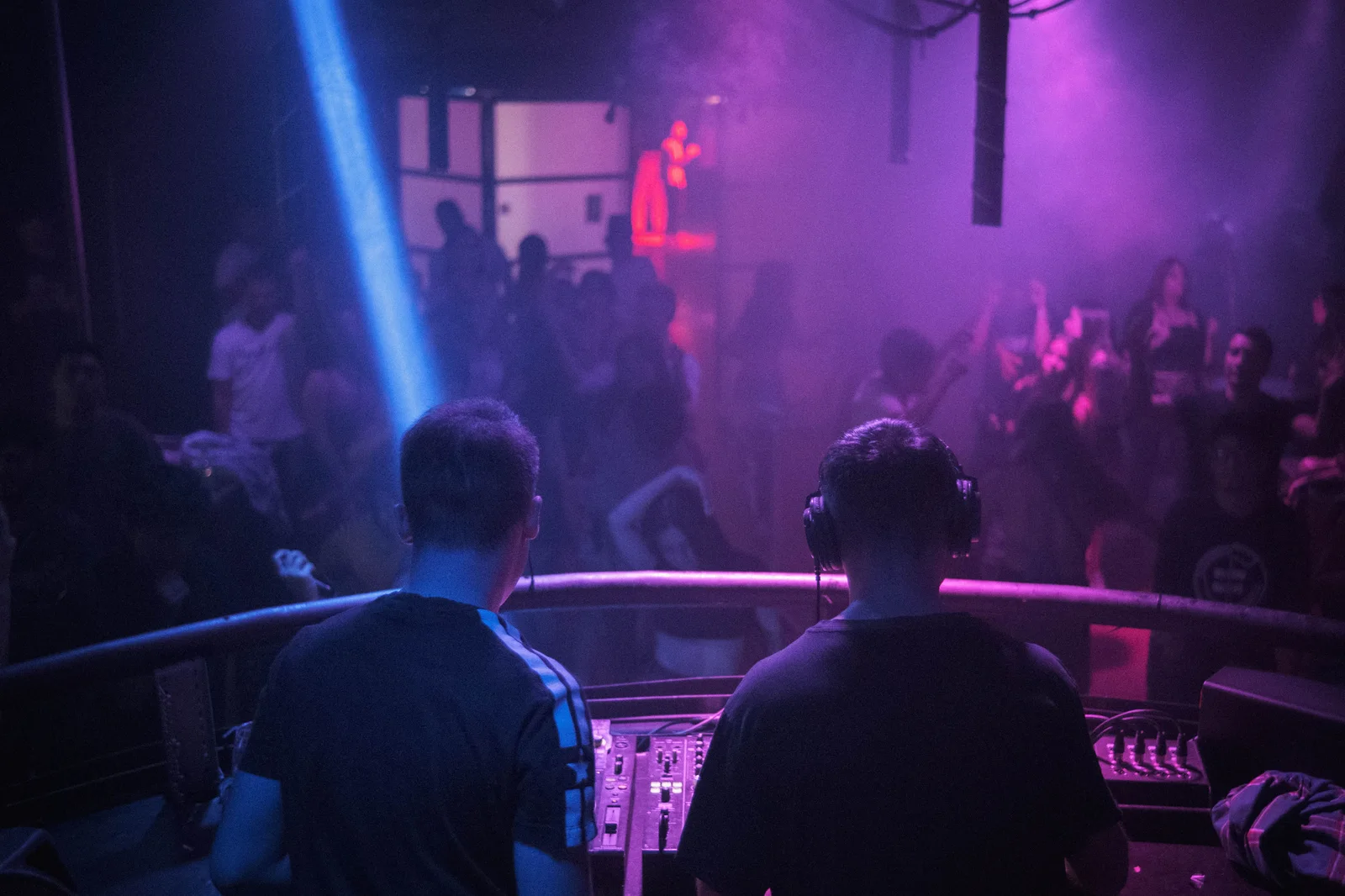A lively night club scene with a DJ mixing music amidst vibrant lights and dancing crowd.