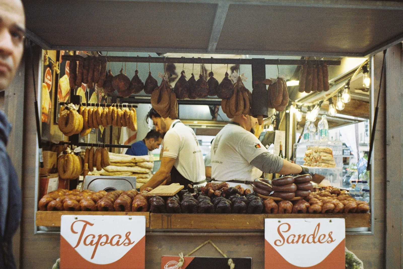 A vibrant scene at a Lisbon market with various meats displayed at a tapas bar.