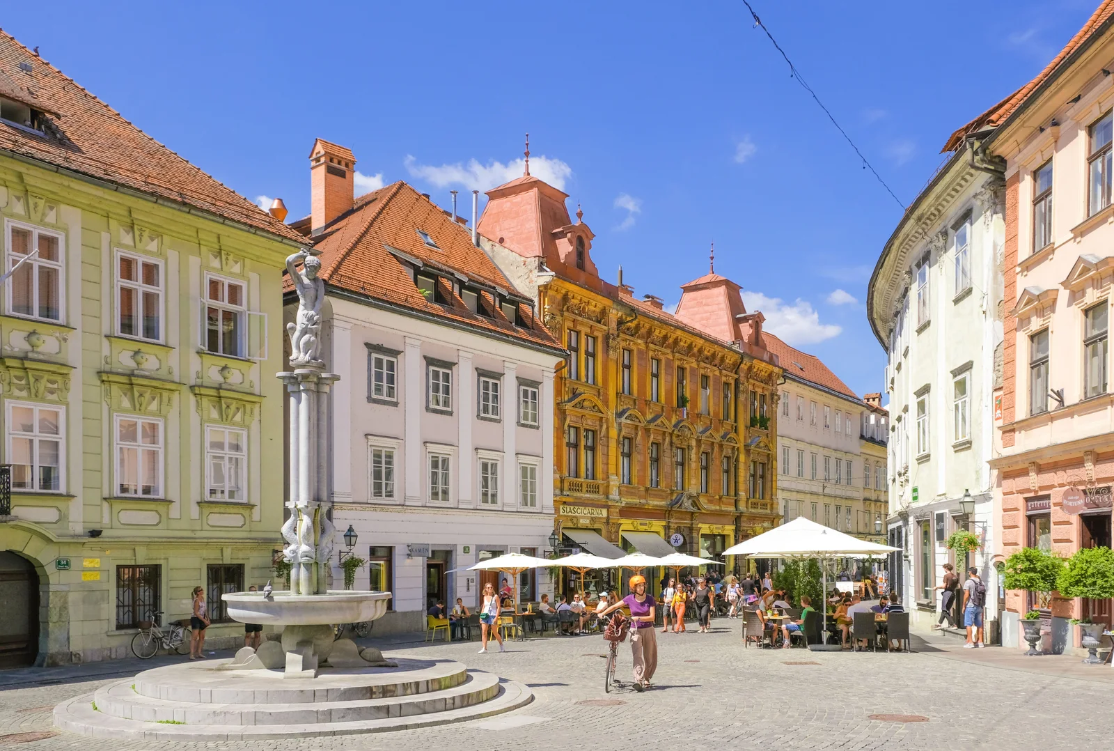 Vibrant square in Ljubljana featuring historic architecture, a fountain, and lively street cafes.