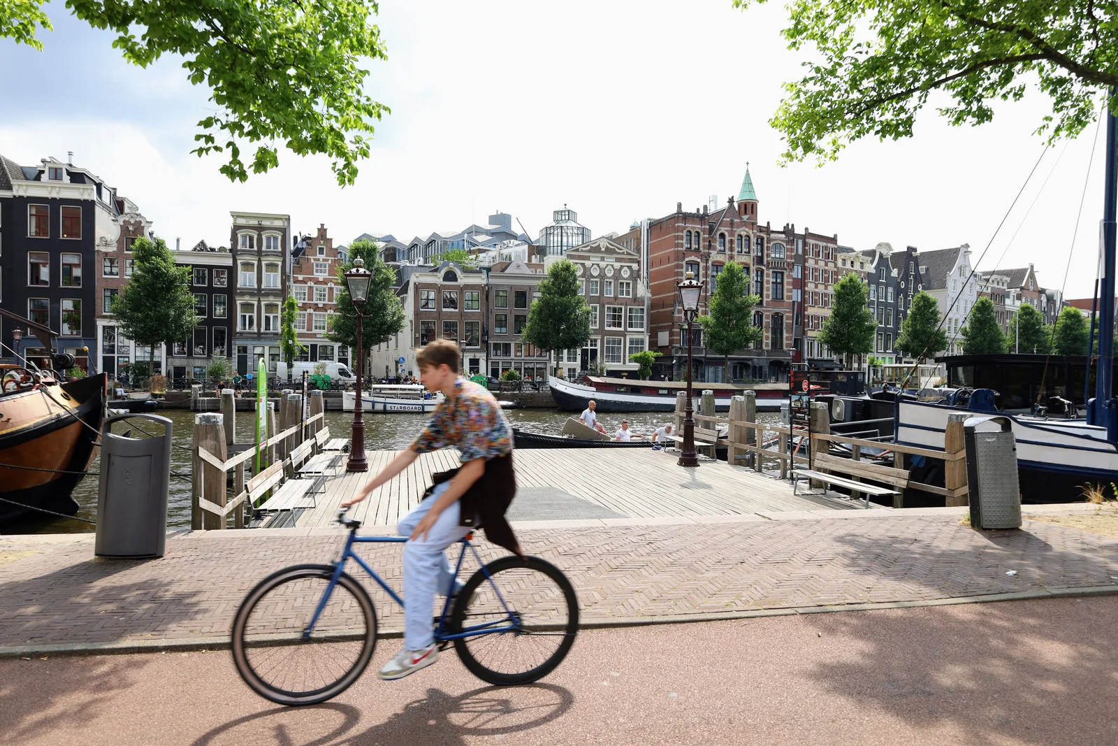 Blurred cyclist passes by picturesque Amsterdam canal with historic buildings in summer.