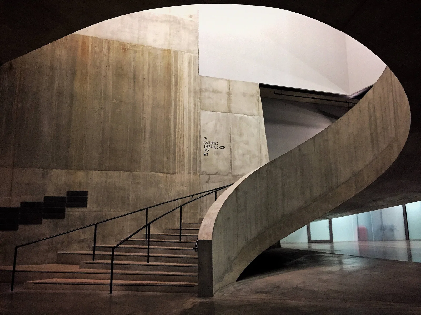 Curved concrete staircase with metal railings in London, showcasing minimalist architecture.